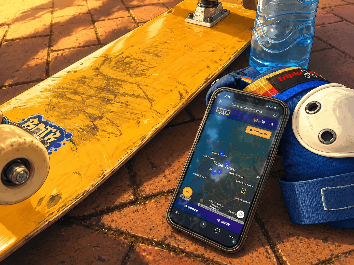 Phone showing the BUTR Spots map and Check In button, propped against pads beside a skateboard